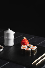 Sushi Set nigiri and sushi rolls in dark stone plate with soy sauce and chopsticks over black background.