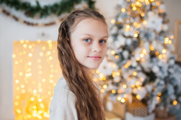Portrait of a beautiful teenage girl in Christmas decorations. Christmas tree, garland and fireplace in the background