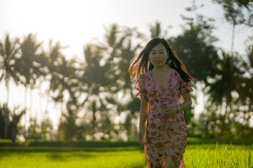 tropical sunset bliss. Young beautiful and attractive Asian Korean woman in elegant dress walking on green rice field enjoying exotic Summer holidays trip in nature