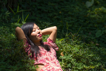 young beautiful and happy Asian Korean woman in stylish dress enjoying adventure holiday trip exploring the beauty of nature at tropical island jungle lying on green