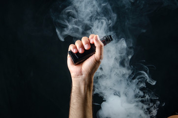 hand holding vape e-cigarette or electronic cigarette with white smoke over a black background. 