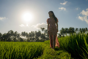 tropical sunset bliss. Young beautiful and attractive Asian Korean woman in elegant dress walking on green rice field enjoying exotic Summer holidays trip in nature