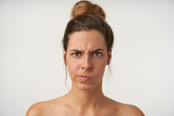 Puzzled attractive young woman with high bun hairstyle standing over white background, looking to...