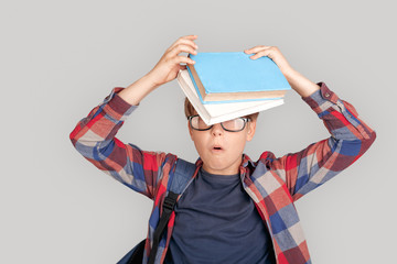 Freestyle. Young boy in glasses standing isolated on grey holding books on head surprised close-up