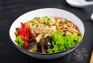 Asian vegan noodles soup with tofu cheese, shimeji mushrooms and fried eggplant in bowl on dark background.