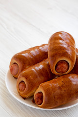 Homemade beef sausage kolache on a white plate on a white wooden table, low angle view. Copy space.