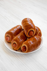 Homemade beef sausage kolache on a white plate on a white wooden surface, low angle view. Close-up.