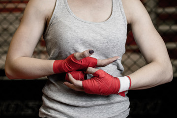 Fototapeta na wymiar Athletic boxer female wraps bandages on her hands puts gloves for fight in gym