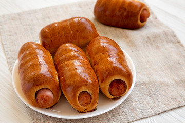 Homemade beef sausage kolache on a white plate on a white wooden background, side view. Close-up.