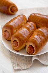 Homemade beef sausage kolache on a white plate on a black background, side view. Close-up.