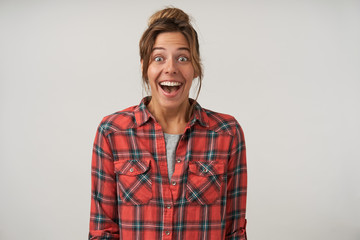 Fototapeta premium Studio shot of surprised pretty young female in checkered shirt, smiling widely to camera with casual hairstyle and natural make-up, isolated over white background