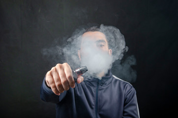 vape and smoke vape electronic e-cigarette or e-cig by a young man with smoke clouds over a black background.