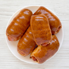 Homemade beef sausage kolache on a white plate on a white wooden table, top view. Flat lay, overhead, from above. Closeup.