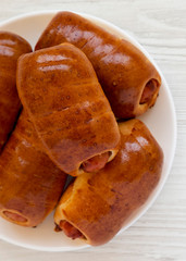 Homemade beef sausage kolache on a white plate on a white wooden background, top view. Close-up.