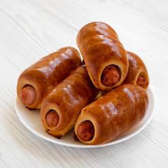 Homemade beef sausage kolache on a white plate on a white wooden background, low angle view. Close-up.