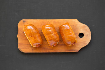Homemade beef sausage kolache on a rustic wooden board on a black surface, top view. Flat lay, overhead, from above, overhead.