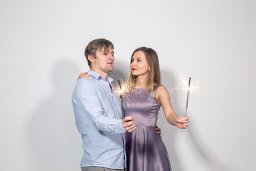 Party, family, christmas, new year and holidays concept - funny couple holding sparklers on white background