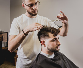 Young man with trendy haircut at barber shop. Barber does the hairstyle and beard trim.
