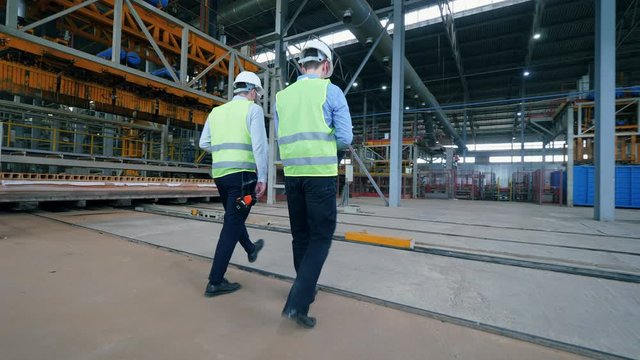 Two male engineers are walking along the industrial factory floor