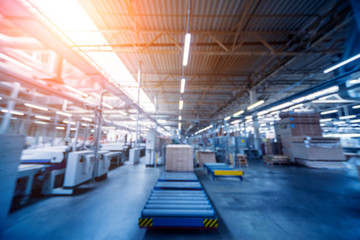 Bloored background of production line of the wooden floor factory. CNC automatic woodworking machine.