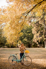 Obraz premium Young woman with bicycle using smartphone in autumn park