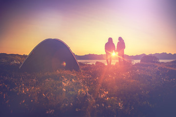 A couple standing holding hands and watching the sunset near tent, travel camping adventure explore the Norway, Lofoten islands