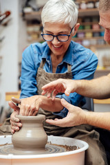 Senior woman spinning clay on a wheel with teacher at pottery class