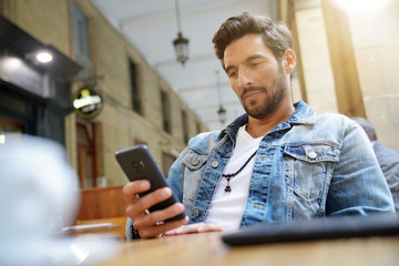 Trendy guy connected on smartphone at coffee shop