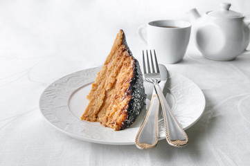 A slice of homemade multilayer biscuit cake. Soaked in butter. Served with chocolate icing and coconut. On a white plate is a fork with a knife. Close-up. White background. 