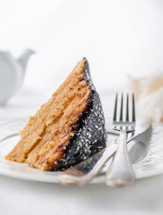 A piece of homemade multi-layer biscuit cake. Soaked in butter cream. Garnished with chocolate icing and coconut. On a white plate with a fork and knife. Close-up. White background. 