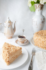 Slice of multilayer Napoleon cake with butter cream. On a white plate. Close-up. Next to a plate is...