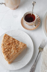 Slice of multilayer Napoleon cake with butter cream. On a white plate. View from above. Near a...