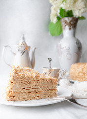 Slice of multilayer Napoleon cake with butter cream. On a white plate. Close-up. Next to a plate is...