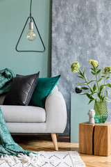Stylish scandinavian interior design of living room with gray sofa, wooden cube, triangle lamp, flowers in vase, colorful pillows and elegant accessories. Abstract background wall, Modern home decor.