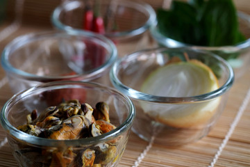 Set of important ingredients for making Stir Fried Mussels with Thai Basil and Chili on wood mat and space for write wording containing Mussels, Onion, Red Chili Paste, Chili and Thai Basil leaves