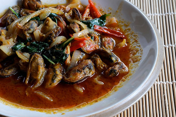 Stir fried mussel with chili paste and sweet basil in ceramic plate on bamboo mat with space for write wording, popular spicy cooked seafood sold in market or restaurant, 