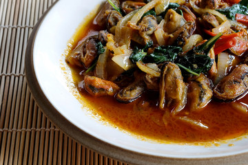 Stir fried mussel with chili paste and sweet basil in ceramic plate on bamboo mat with space for write wording, popular spicy cooked seafood sold in market or restaurant, 