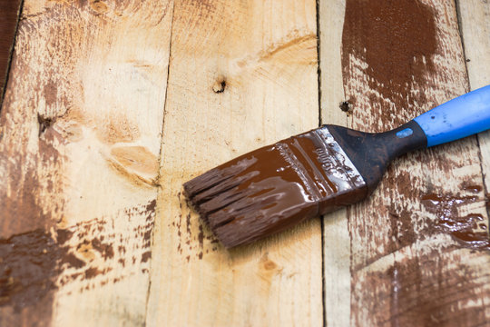 A paintbrush on wood covered in brown paint