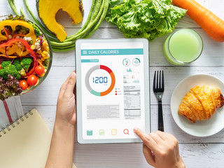 Calories counting , diet , food control and weight loss concept. woman using Calorie counter application on tablet at dining table with fresh vegetable salad - obrazy, fototapety, plakaty