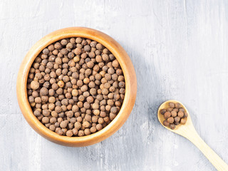 Allspice (Jamaica pepper) in a wooden cup and spoon on a gray background