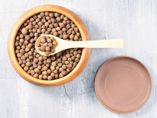 Allspice (Jamaica pepper) in a wooden cup with spoon and clay plate on a gray background