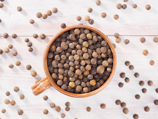 Allspice (Jamaica pepper) in a clay cup on a brown wooden background
