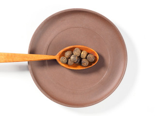 Allspice (Jamaica pepper) in the clay plate and wooden spoon horizontally on white background