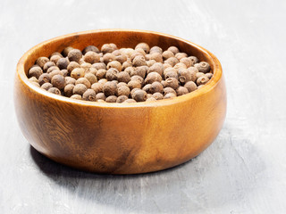 Allspice (Jamaica pepper) in the wooden cup on gray cement background