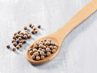Allspice (Jamaica pepper) in the wooden spoon diagonally on gray cement background
