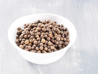 Allspice (Jamaica pepper) in white cup on grey background