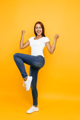 Full length portrait of cheerful young woman celebrating success isolated on yellow background