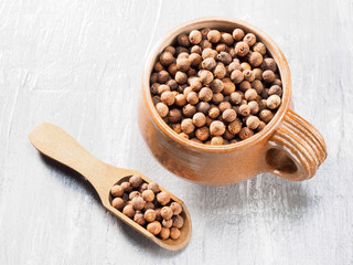 Allspice (Jamaica pepper) in clay cup and on wooden scoop diagonally on grey cement background