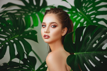 Portrait of young and beautiful woman with perfect smooth skin in tropical leaves.