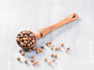 Allspice (Jamaica pepper) wooden spoon diagonally on grey cement background
